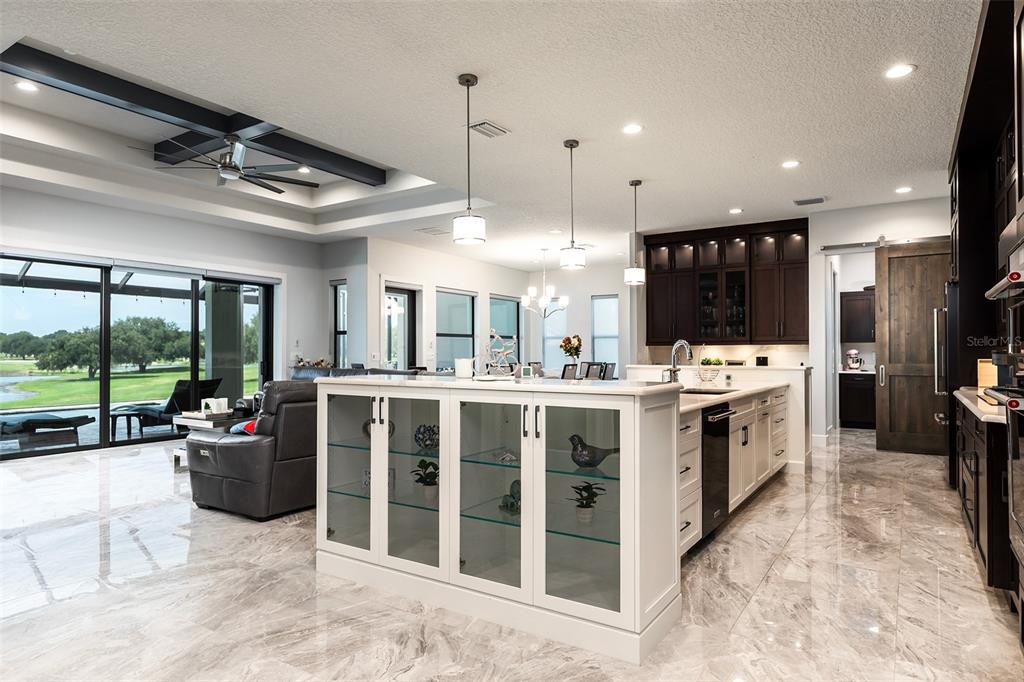 A bright kitchen features white cabinets, a glass-front island, and marble flooring overlooking a patio — 14941 GREEN VALLEY BOULEVARD, CLERMONT, FL