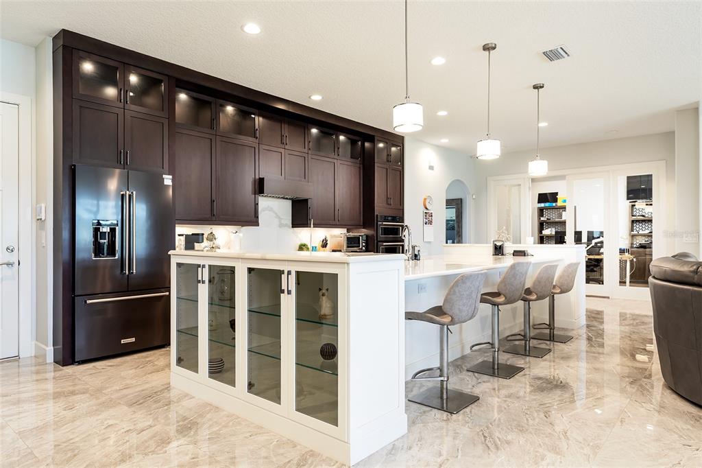 A modern kitchen features dark wood cabinets, a white island with glass-front cabinets, and tile flooring — 14941 GREEN VALLEY BOULEVARD, CLERMONT, FL
