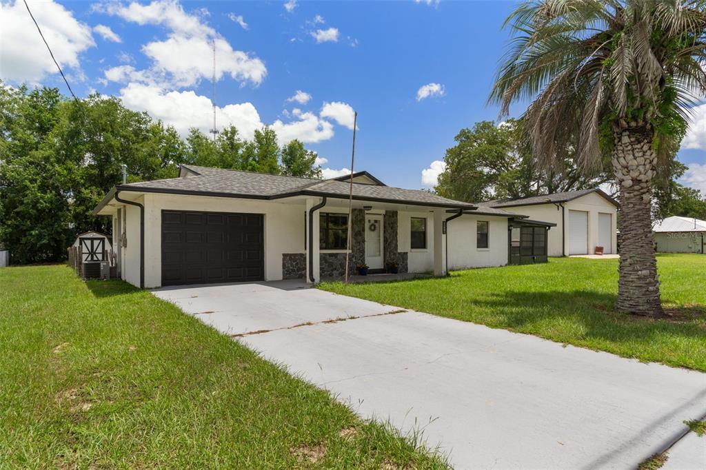 A single-story house with a white exterior, dark garage door, and a detached garage — 11891 SE 84TH AVENUE, BELLEVIEW, FL