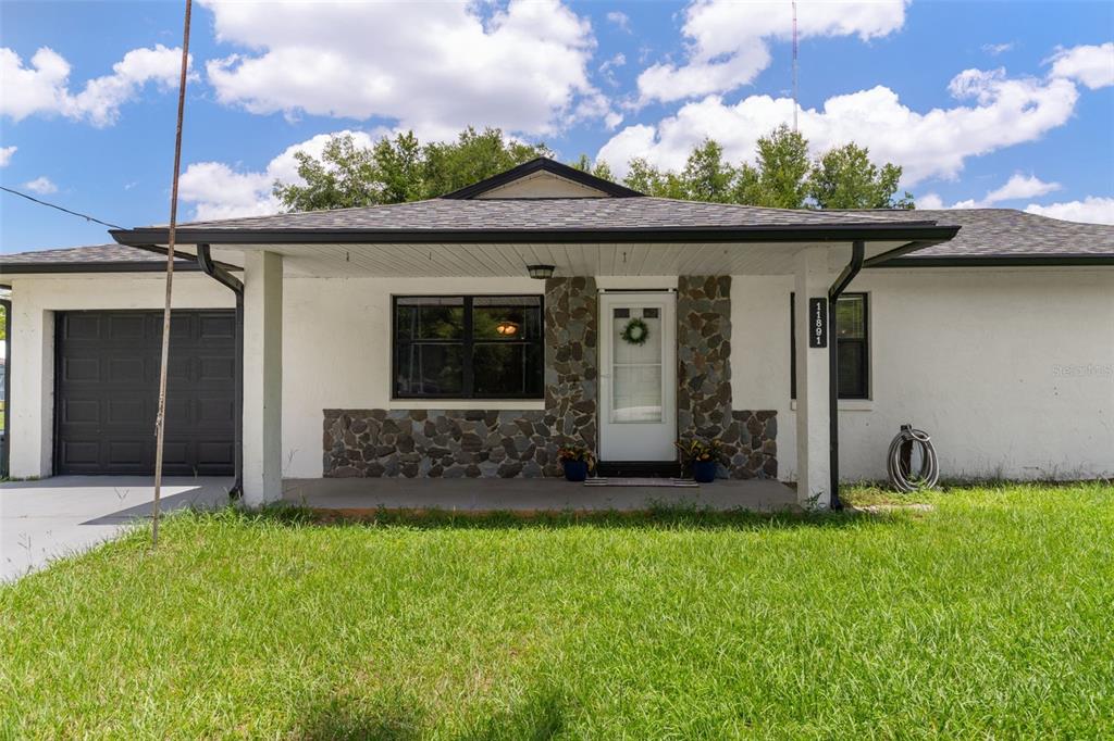 A single-story house with a white stucco exterior, stone accents, and a covered front porch — 11891 SE 84TH AVENUE, BELLEVIEW, FL