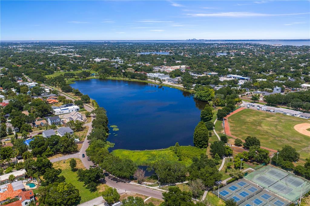 An aerial view shows a large lake surrounded by residential homes, trees, and sports courts — 1175 HIGHLAND COURT N, ST PETERSBURG, FL