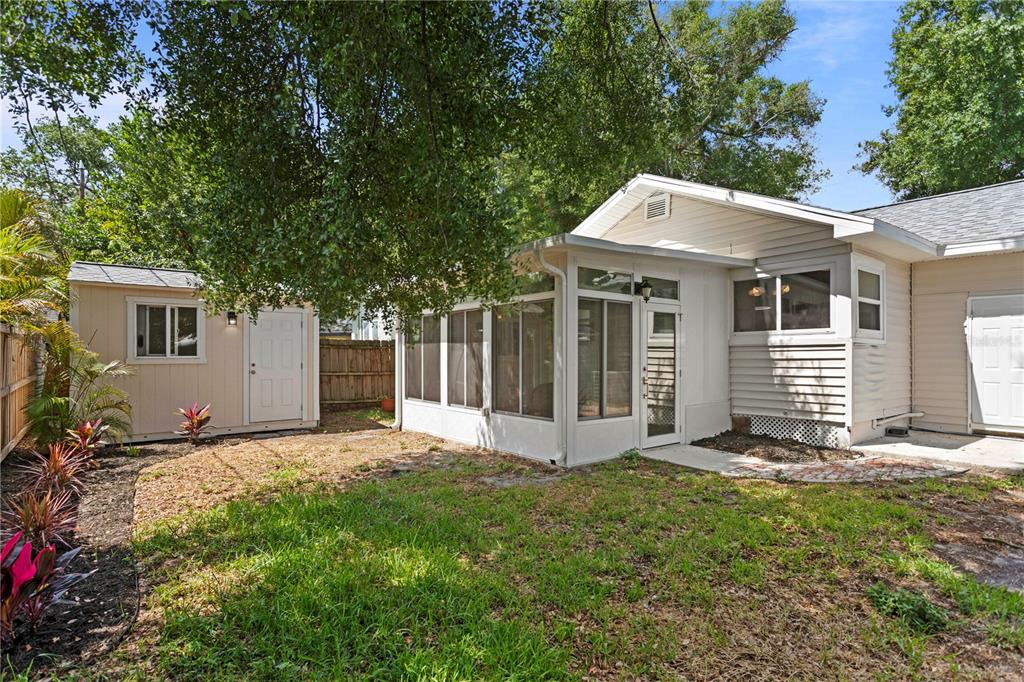 A backyard features a light-colored shed, a screened-in porch, and a grassy lawn with landscaping — 1175 HIGHLAND COURT N, ST PETERSBURG, FL