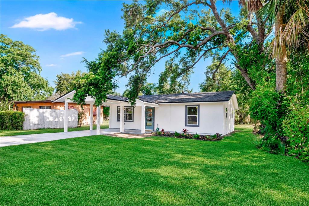 A white single-story house with a carport sits on a green lawn under large trees — 483 PENNSYLVANIA AVENUE, WINTER GARDEN, FL