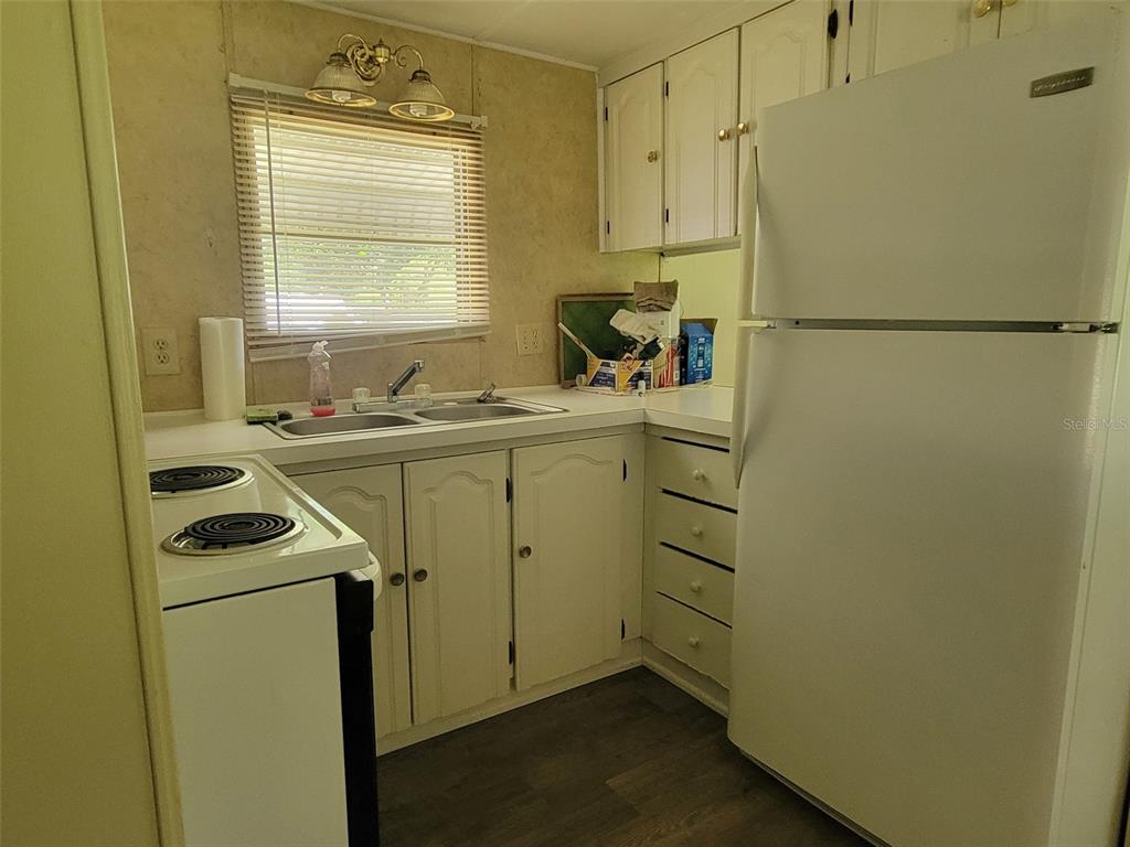 A small kitchen features white cabinets, a double sink, a stove, and a refrigerator — 3399 SE 93RD PLACE, OCALA, FL