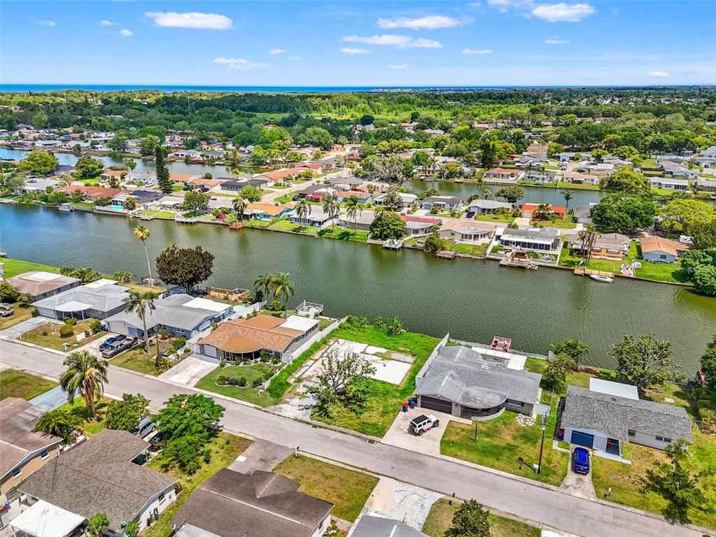 An aerial view shows a residential neighborhood with houses lining a canal leading toward the ocean — 4101 BADEN DRIVE, HOLIDAY, FL