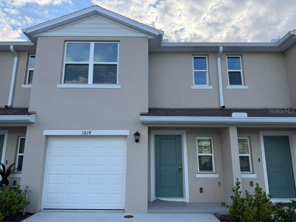 A two-story townhouse exterior features a single-car garage, a teal front door, and beige siding — 1814 LINDENS STREET, KISSIMMEE, FL