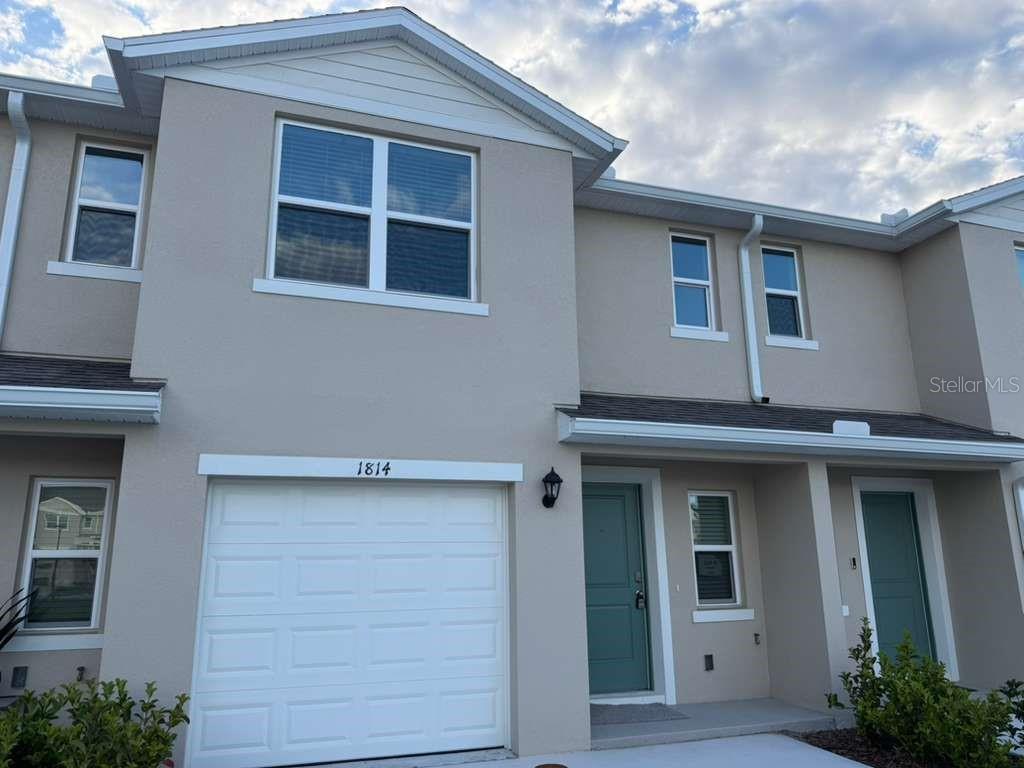 A two-story townhouse exterior features a white garage door, light-colored stucco walls, and teal doors — 1814 LINDENS STREET, KISSIMMEE, FL