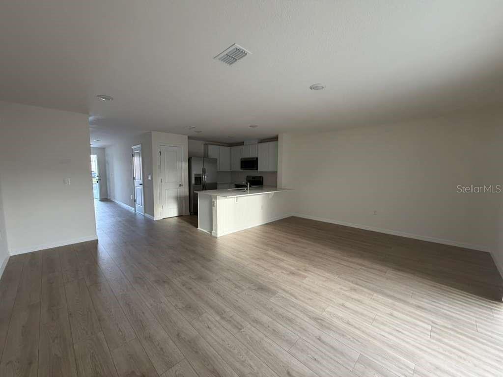 An open-concept living area features light wood-look flooring and a kitchen with white cabinets — 1814 LINDENS STREET, KISSIMMEE, FL