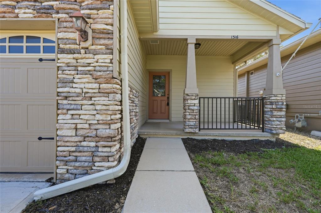 A concrete walkway leads to a covered front porch with stone pillars and a door — 1316 NW 120TH WAY, GAINESVILLE, FL