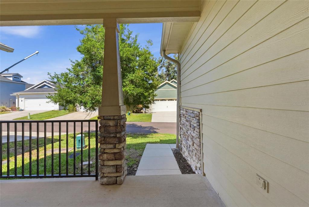 A covered front porch features a stone-based pillar, metal railing, and light-colored horizontal siding — 1316 NW 120TH WAY, GAINESVILLE, FL