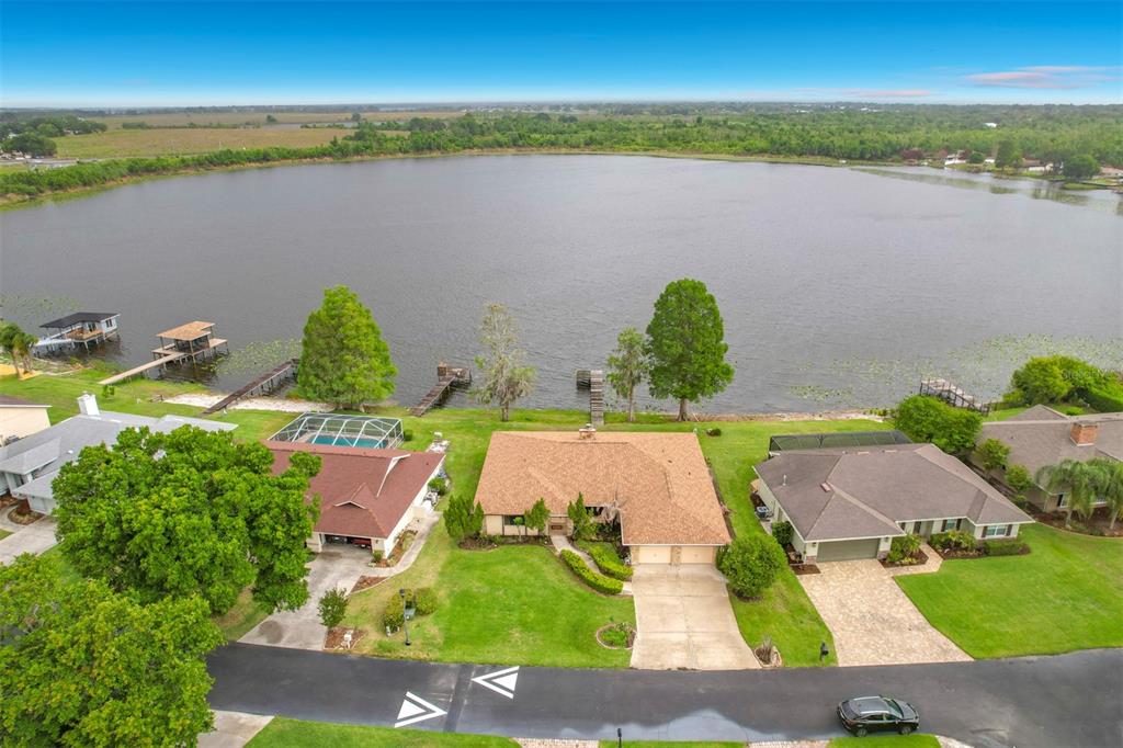 An aerial view shows three suburban houses situated along the shore of a large lake — 247 S LAKE PANSY DRIVE, WINTER HAVEN, FL