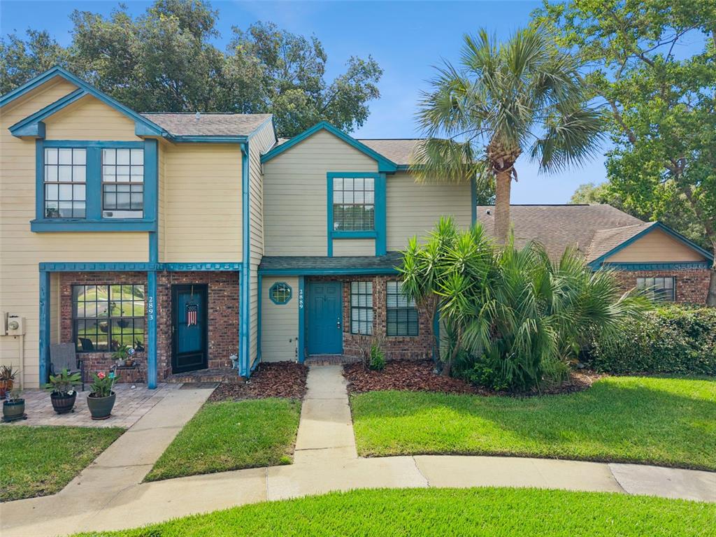 A two-story townhouse with brick and siding exterior, a teal front door, and palm trees — 2889 WAREHAM COURT, CASSELBERRY, FL