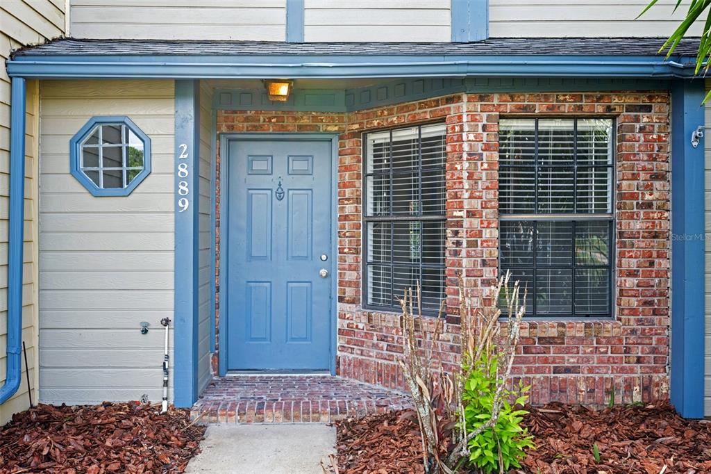 A blue front door is centered between a brick bay window and a small octagonal window — 2889 WAREHAM COURT, CASSELBERRY, FL