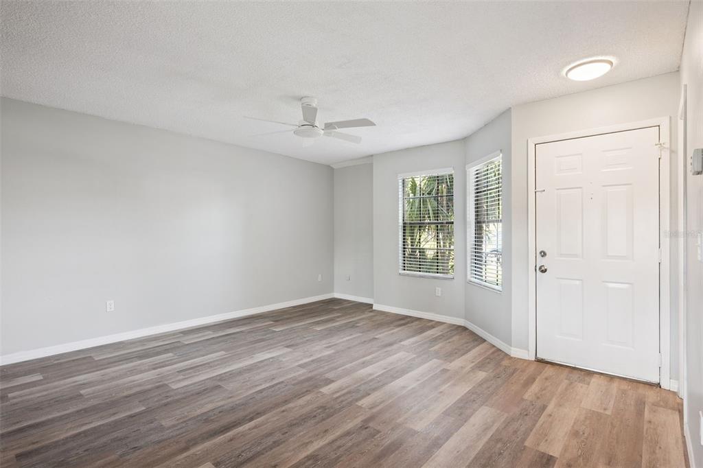 An empty living room features light gray walls, wood-look flooring, a ceiling fan, and windows — 2889 WAREHAM COURT, CASSELBERRY, FL
