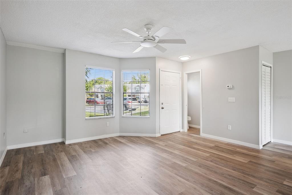 An empty living room features light gray walls, wood-look flooring, a ceiling fan, and windows — 2889 WAREHAM COURT, CASSELBERRY, FL