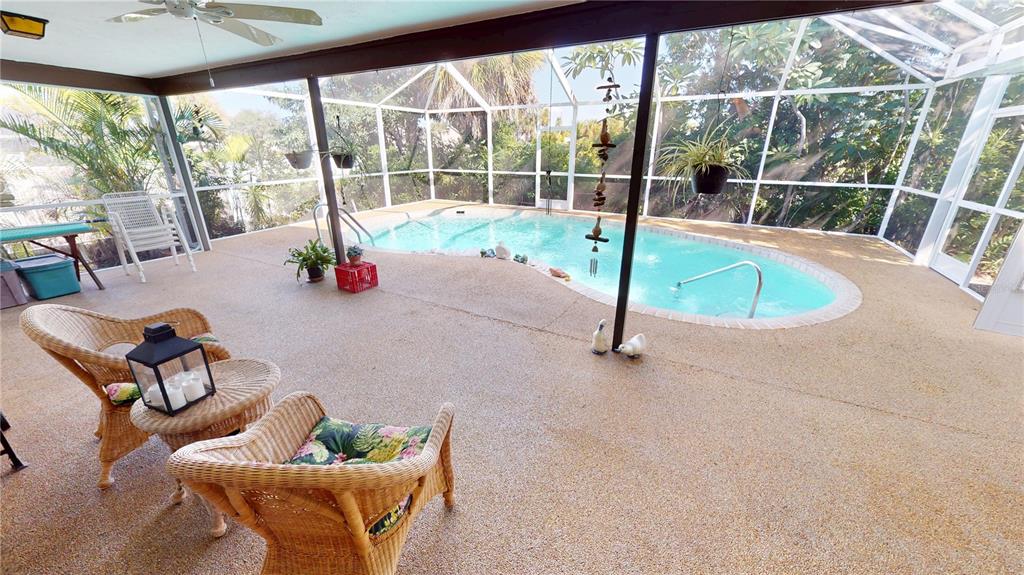 A covered patio features a swimming pool, wicker furniture, and a screened-in enclosure — 18422 BURKHOLDER CIRCLE, PORT CHARLOTTE, FL