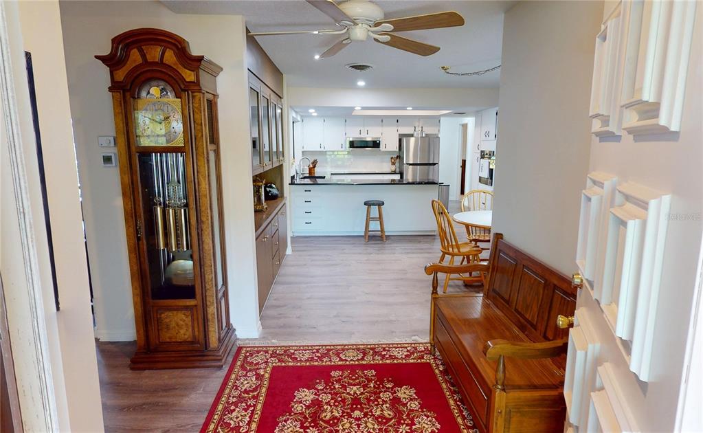 A view from a hallway into a kitchen featuring a grandfather clock and wooden bench — 18422 BURKHOLDER CIRCLE, PORT CHARLOTTE, FL
