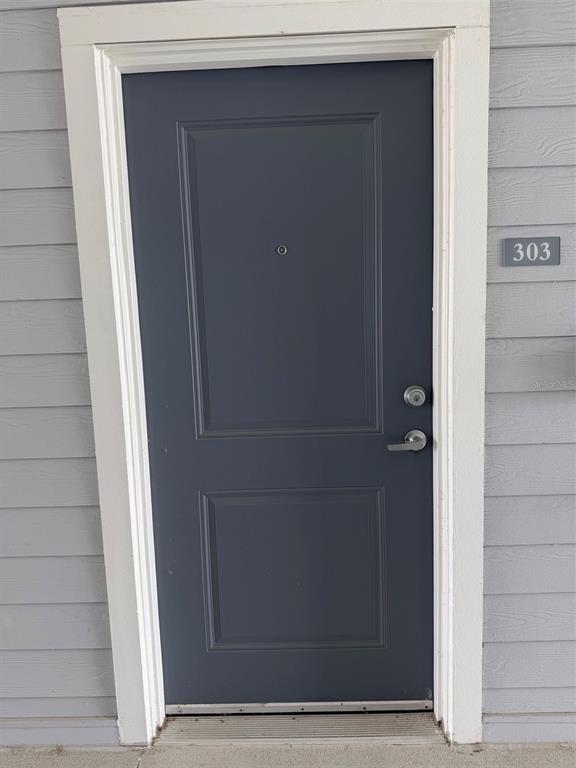A dark gray apartment door with a silver handle and a peephole, labeled number 303 — 510 ACADEMY DRIVE UNIT 303, KISSIMMEE, FL