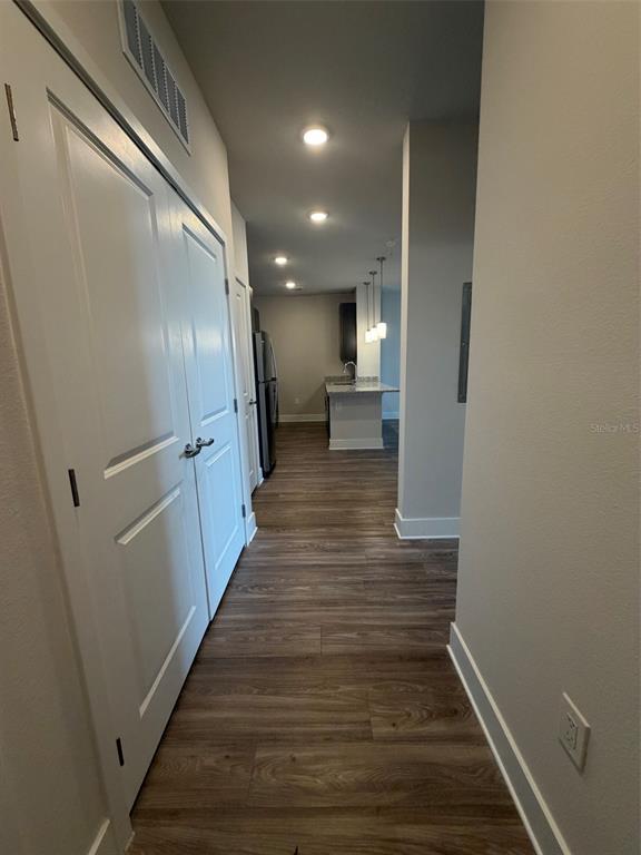 A hallway with wood-look flooring leads to an open kitchen with a center island — 510 ACADEMY DRIVE UNIT 303, KISSIMMEE, FL