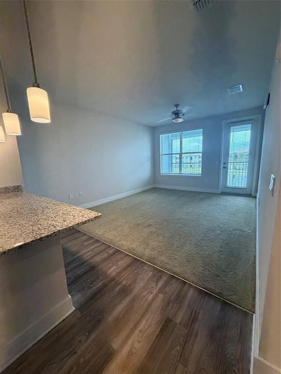 An open-concept living area features wood-look flooring, a granite-topped island, and a carpeted living space — 510 ACADEMY DRIVE UNIT 303, KISSIMMEE, FL