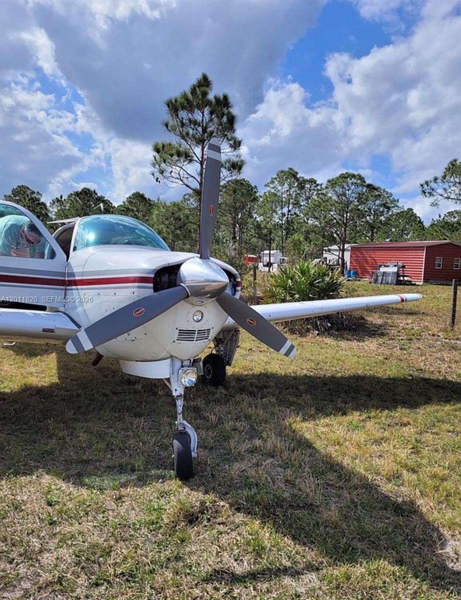 A small, white, single-engine airplane is parked on a grassy field near a red building — 1000 NE 365 Lane, Okeechobee FL 34972, OKEECHOBEE, FL
