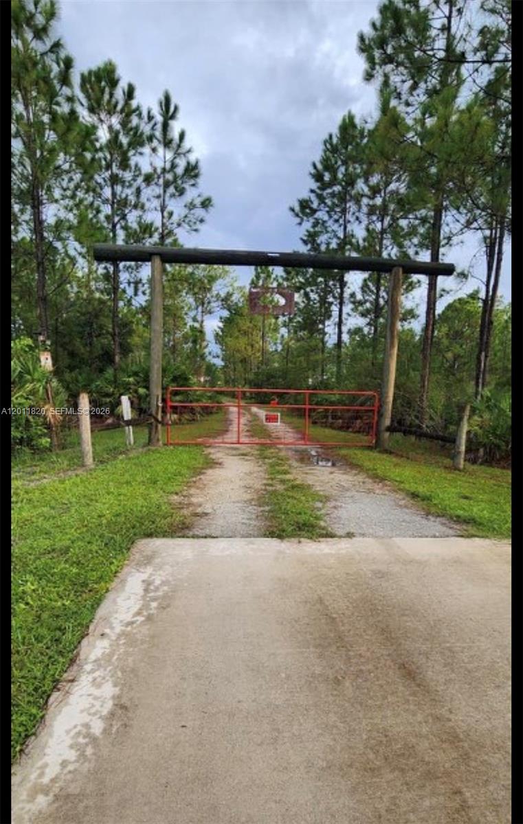 A red metal gate stands at the entrance of a dirt driveway surrounded by trees — 1000 NE 365 Lane, Okeechobee FL 34972, OKEECHOBEE, FL