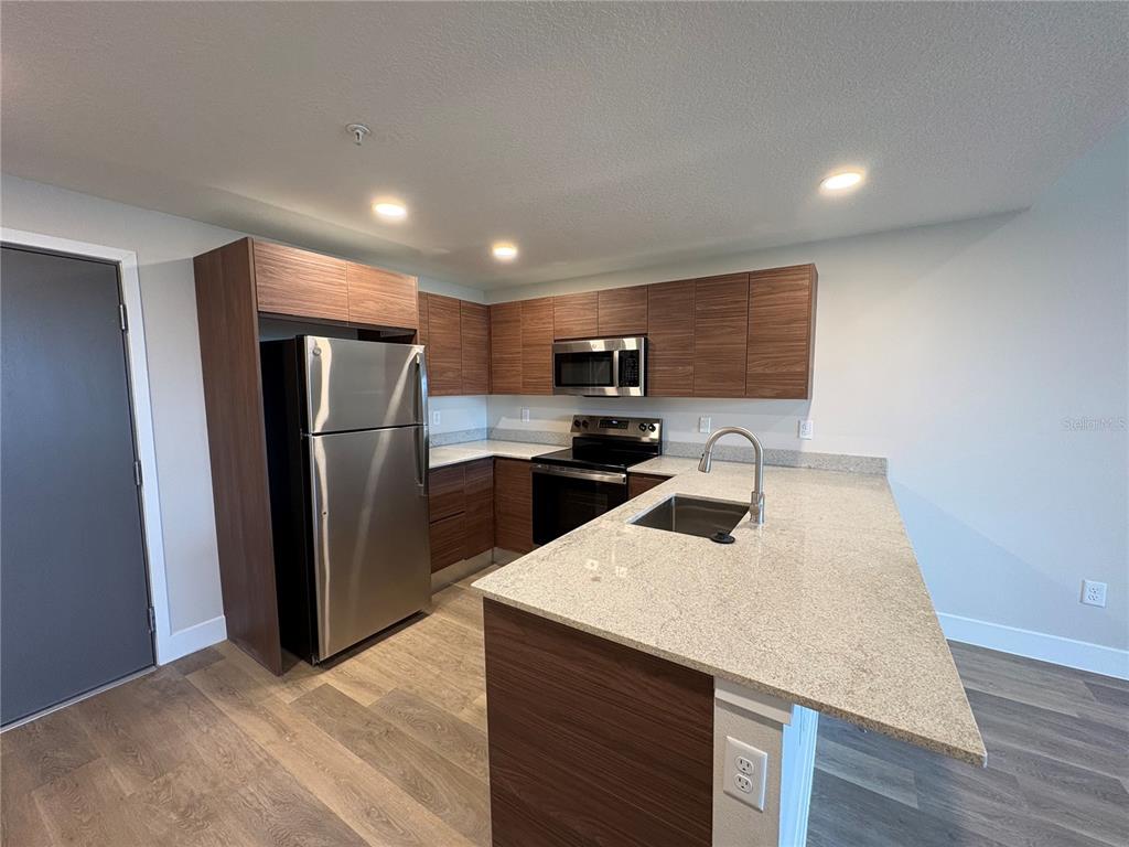 A modern kitchen features wood-grain cabinets, stainless steel appliances, and a granite-topped island — 4424 S TEXAS AVENUE UNIT 1-218, ORLANDO, FL