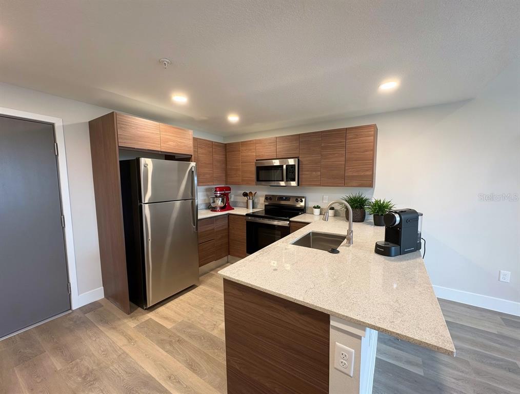 A modern kitchen features wood-grain cabinets, stainless steel appliances, and a granite-topped island — 4424 S TEXAS AVENUE UNIT 1-218, ORLANDO, FL