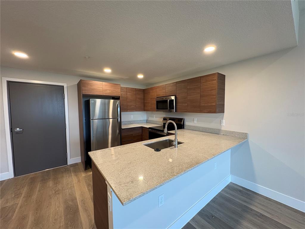 A modern kitchen features wood-grain cabinets, stainless steel appliances, and a granite-topped island with sink — 4424 S TEXAS AVENUE UNIT 1-218, ORLANDO, FL
