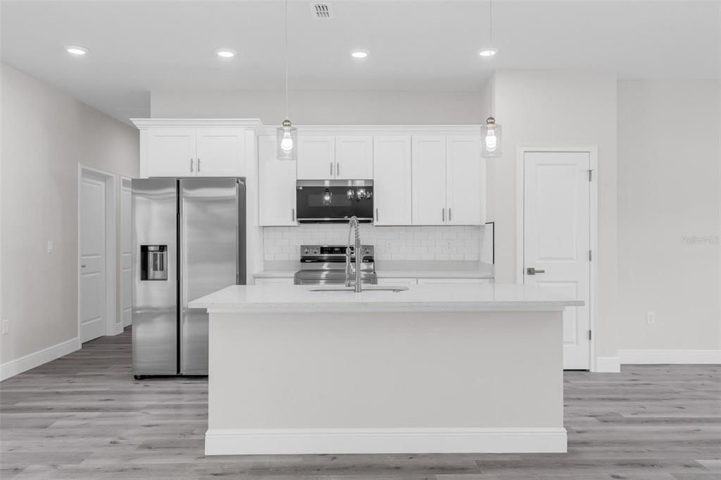 A modern kitchen features white cabinetry, stainless steel appliances, a center island, and gray flooring — 1028 W CITRUS SPRINGS BOULEVARD, CITRUS SPRINGS, FL