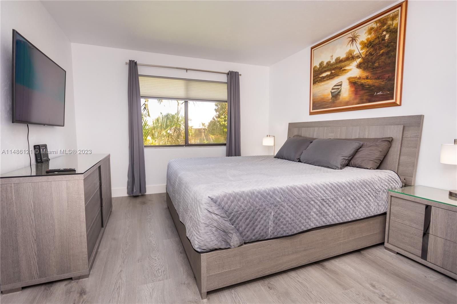 A bedroom features a gray bed, matching furniture, a wall-mounted television, and a landscape painting — 500 N Francisco St # 234, Clewiston FL 33440, CLEWISTON, FL