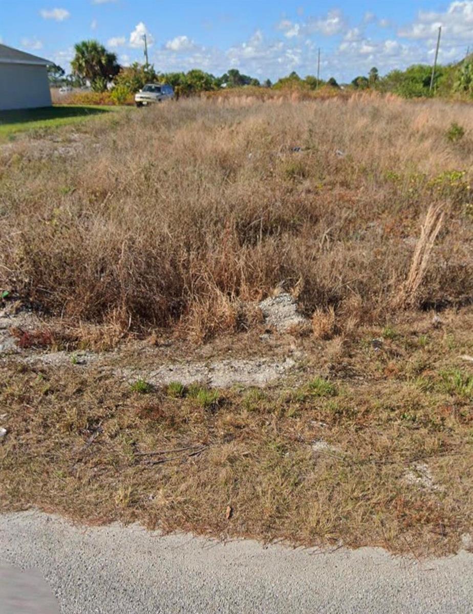A vacant, grass-covered residential lot sits next to a house under a blue sky — 9024 W Justice Circle, FL 33935, FL