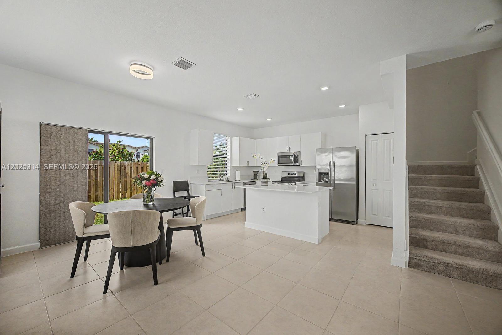 A bright kitchen and dining area features white cabinetry, stainless steel appliances, and carpeted stairs — 13170 SW 232nd Ln, Miami FL 33032, MIAMI, FL