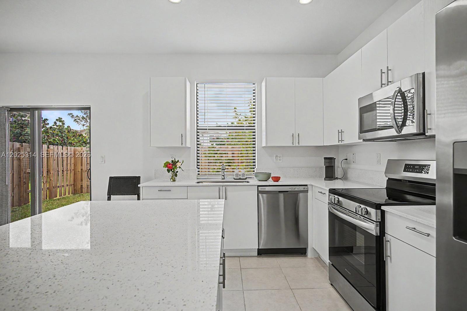 A modern kitchen features white cabinets, stainless steel appliances, quartz countertops, and a sliding glass door — 13170 SW 232nd Ln, Miami FL 33032, MIAMI, FL