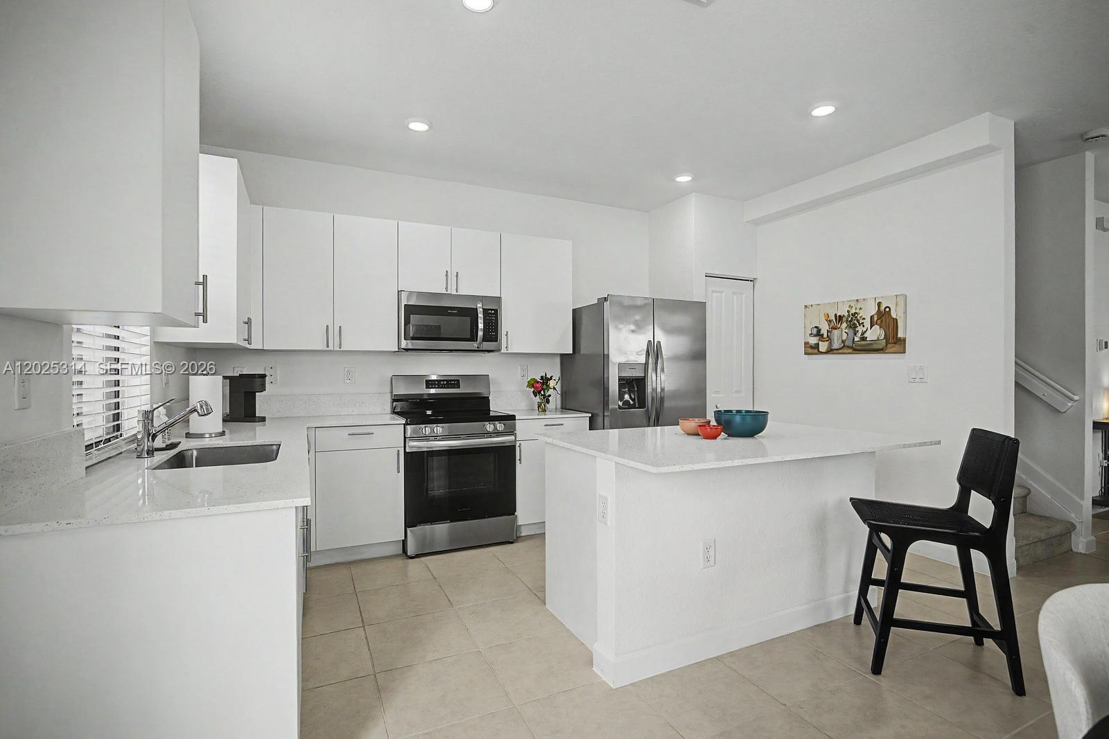 A modern kitchen features white cabinetry, stainless steel appliances, a quartz island, and tile flooring — 13170 SW 232nd Ln, Miami FL 33032, MIAMI, FL