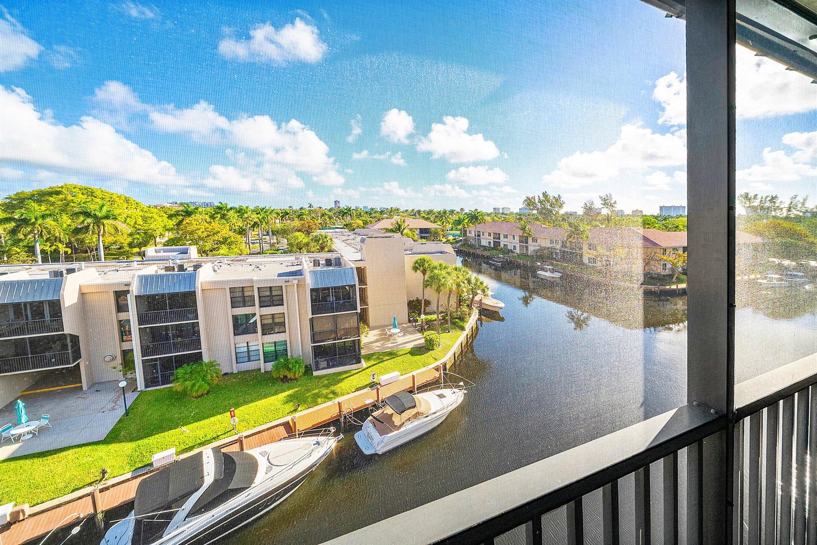 A view from a screened balcony overlooking a canal with docked boats and apartment buildings — 6 Royal Palm Way # 605, Boca Raton FL 33432, BOCA RATON, FL