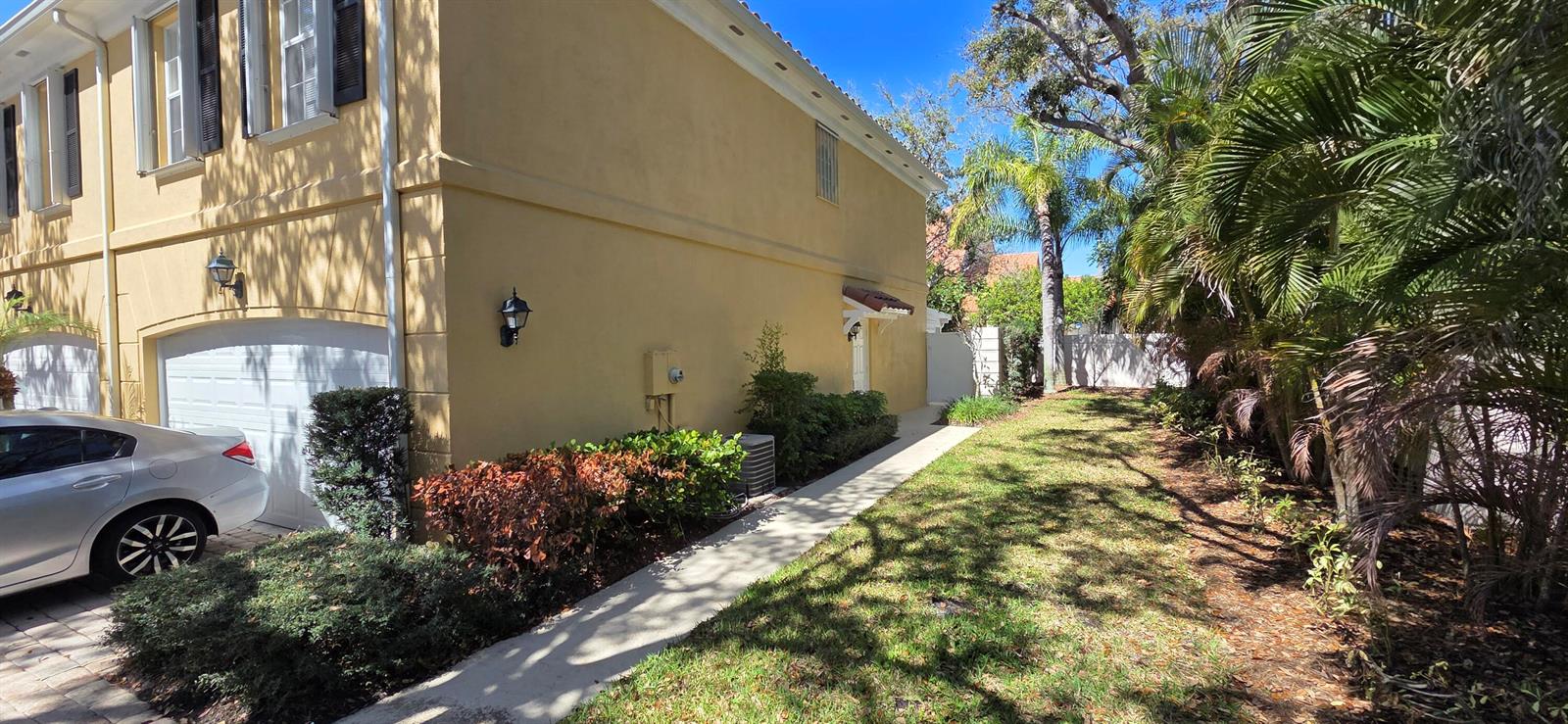 A side view of a yellow two-story townhouse with a garage and a grassy yard — TEQUESTA, FL
