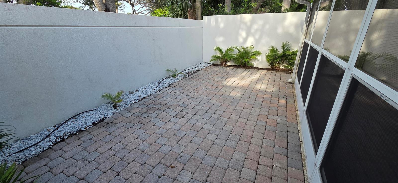 A paved patio area features a white privacy wall, small palm plants, and screened enclosure — TEQUESTA, FL