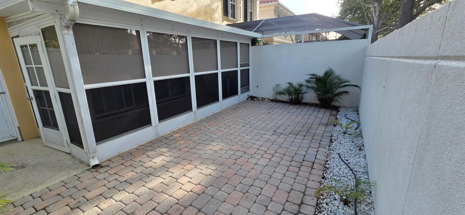 A paved patio area sits beside a screened-in porch and a white privacy wall — TEQUESTA, FL