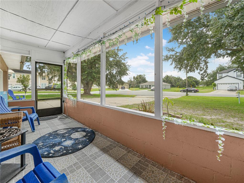 A screened-in porch with tiled flooring, blue chairs, and a view of a suburban street — 5 TUNA LANE, POINCIANA, FL
