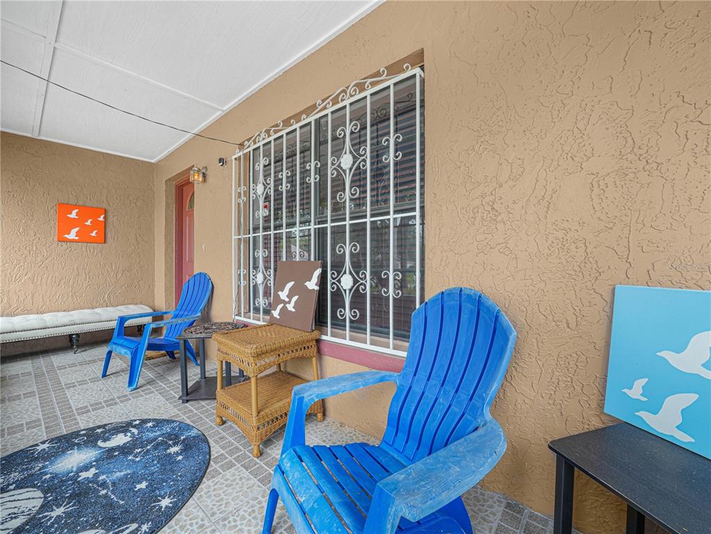 A covered porch features two blue Adirondack chairs, a wicker side table, and a window grate — 5 TUNA LANE, POINCIANA, FL