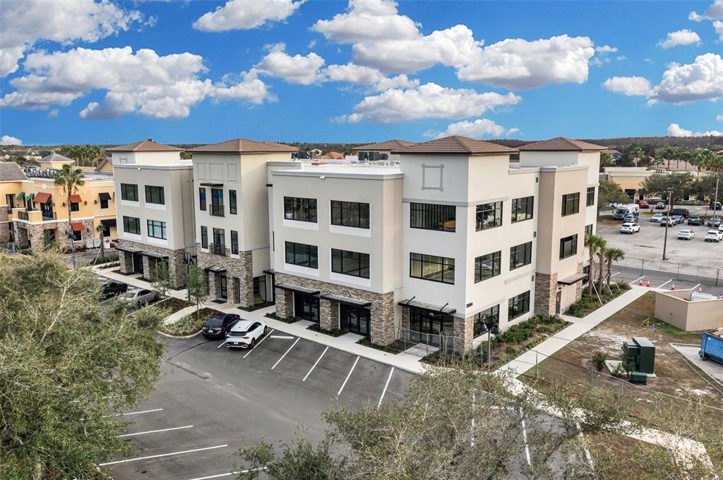An aerial view of a three-story commercial building with a parking lot and landscaping — 13564 VILLAGE PARK DRIVE UNIT 215, ORLANDO, FL