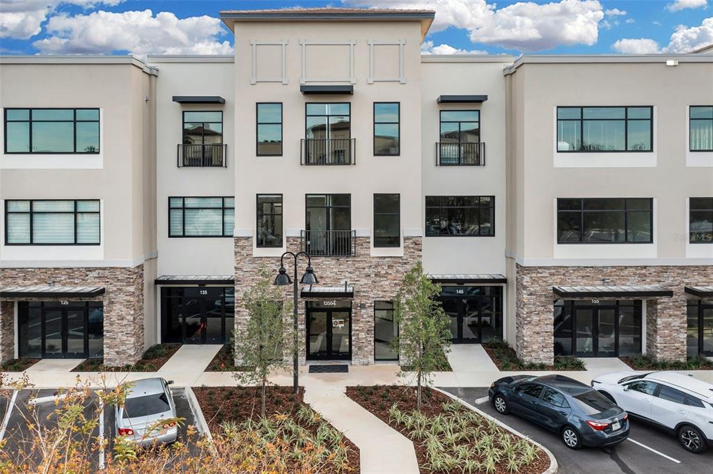 A three-story commercial building features a stone facade, glass storefronts, and a paved parking lot — 13564 VILLAGE PARK DRIVE UNIT 215, ORLANDO, FL
