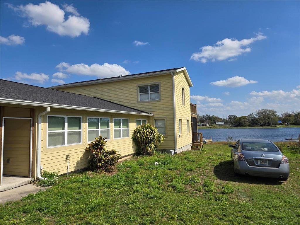 A two-story yellow house with a dark roof sits next to a lake — 8725 TWIN LAKES BOULEVARD, TAMPA, FL