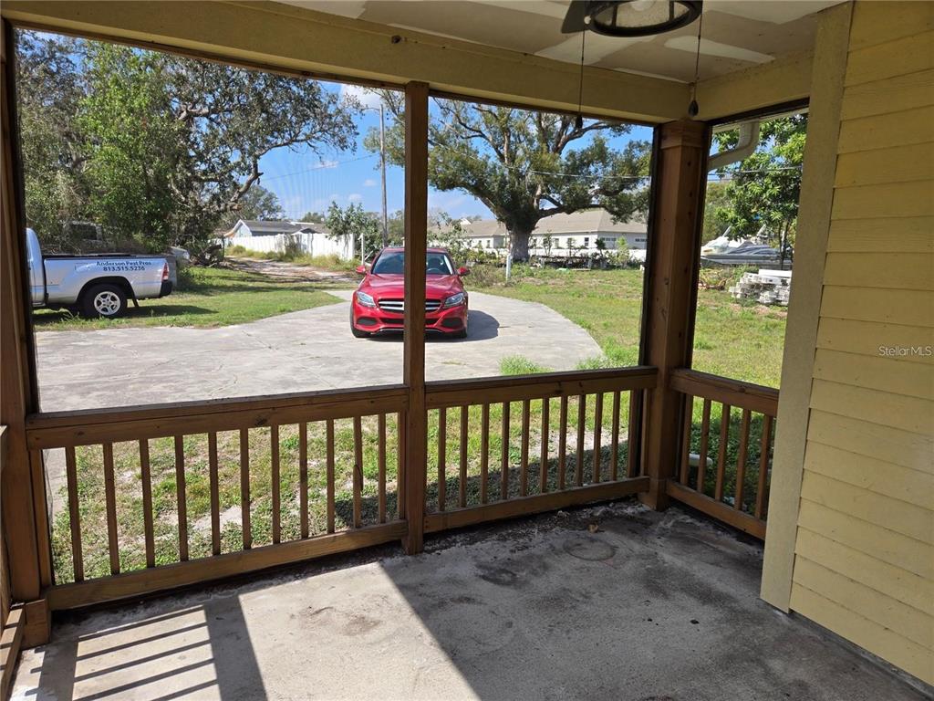 A screened-in porch with a concrete floor and wooden railing overlooks a driveway and yard — 8725 TWIN LAKES BOULEVARD, TAMPA, FL