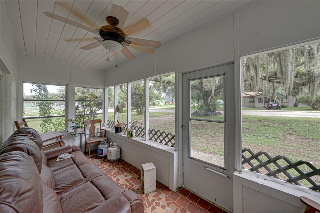A screened-in porch features a brown leather sofa, tiled floor, ceiling fan, and exterior views — 1000 ALTON STREET, AVON PARK, FL