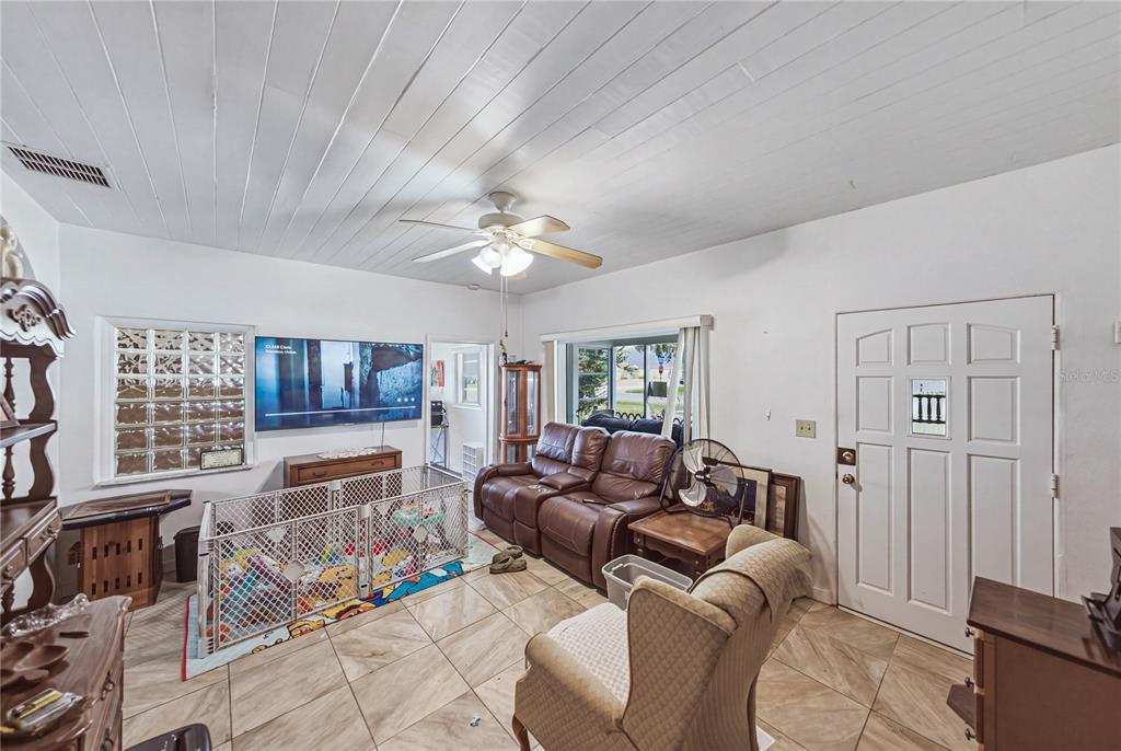 A living room features tile floors, a white wood-paneled ceiling, a ceiling fan, and furniture — 1000 ALTON STREET, AVON PARK, FL