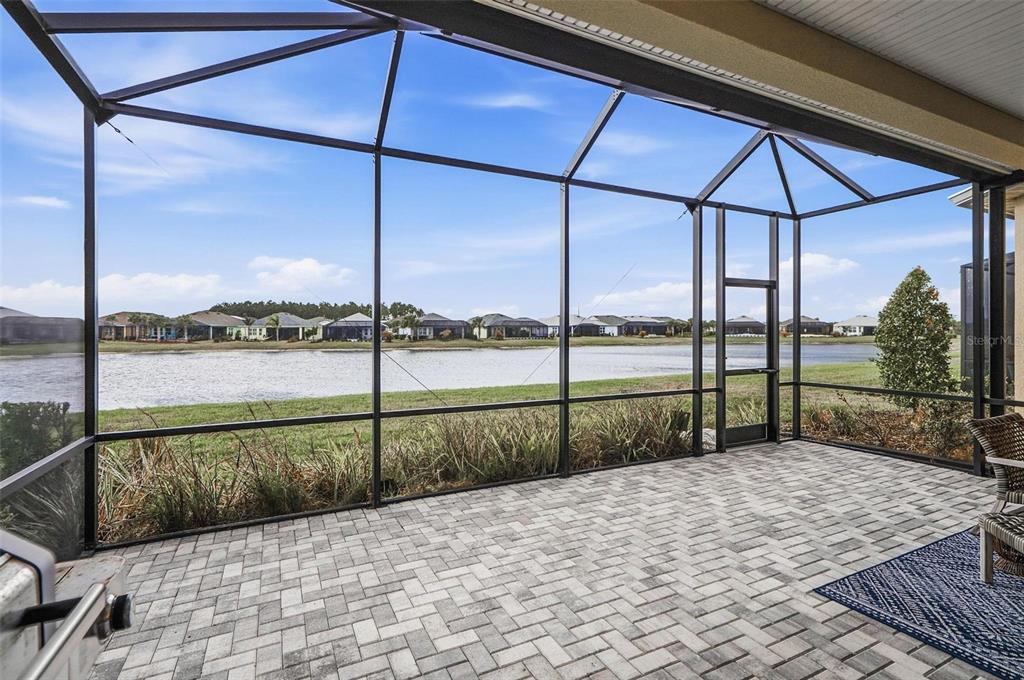 A screened-in patio with paver flooring overlooks a lake and neighboring houses — 281 MARGARITAVILLE AVENUE, DAYTONA BEACH, FL