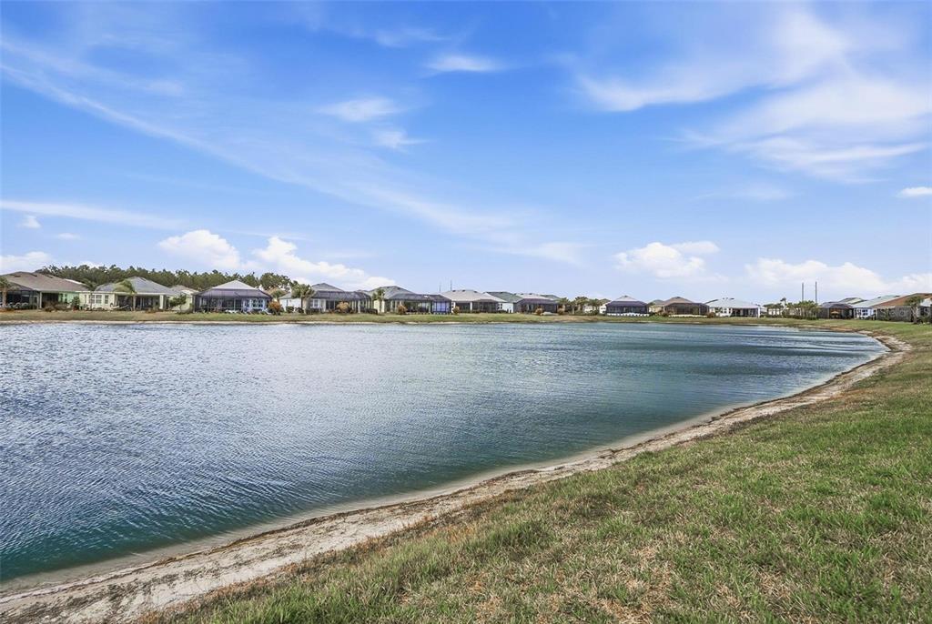 A wide view of a residential pond surrounded by houses under a blue sky — 281 MARGARITAVILLE AVENUE, DAYTONA BEACH, FL