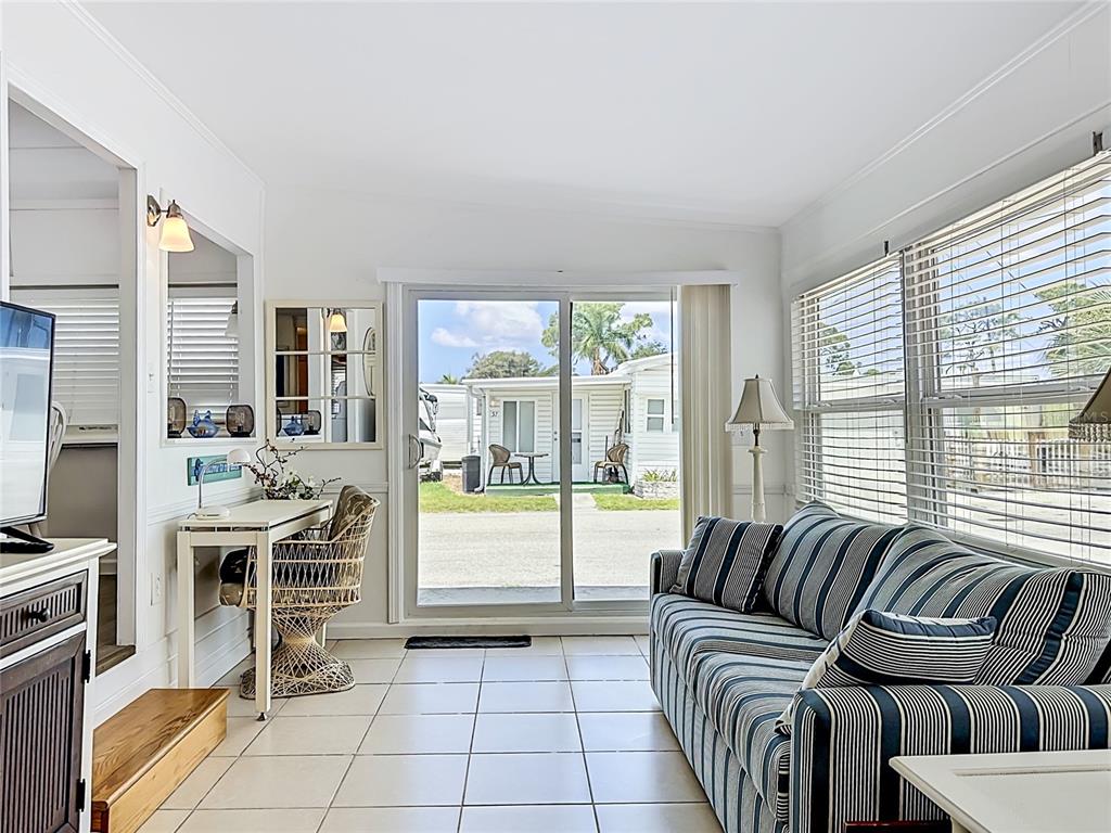 A living room with tile floors, a striped sofa, a desk, and sliding glass doors — 10315 CORTEZ ROAD W UNIT 58-3, BRADENTON, FL